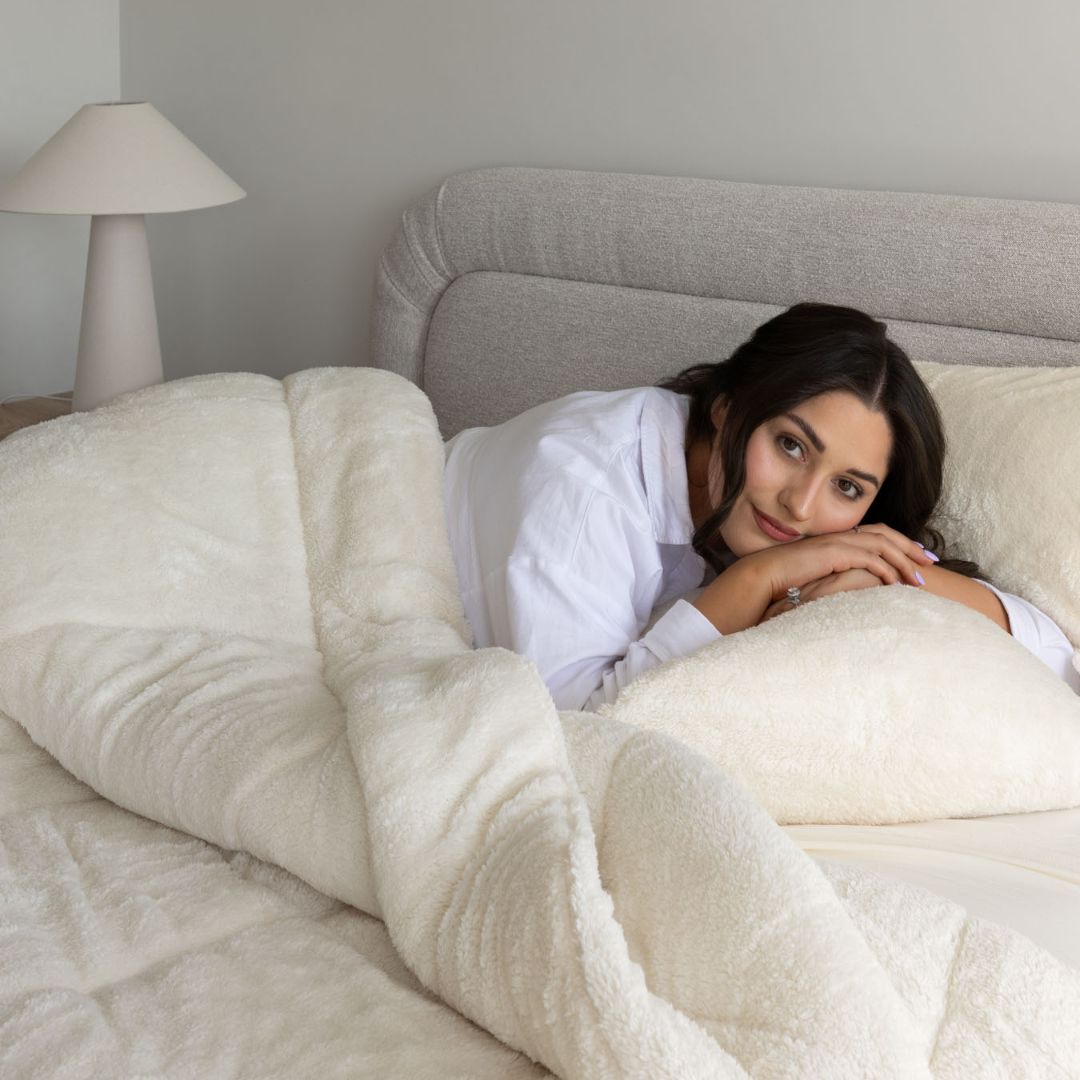 Woman in a robe lying in bed under a white comforter, with a lamp in the background.