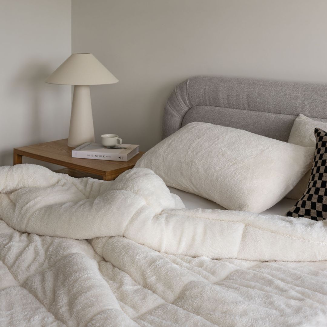 Neatly made bed with white bedding and gray headboard, side table with lamp and books.