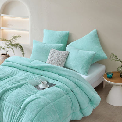 Turquoise bedding set on a bed in a bedroom with a side table and plants.