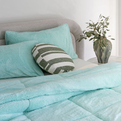 Bed with teal bedding and pillows in a bedroom setting