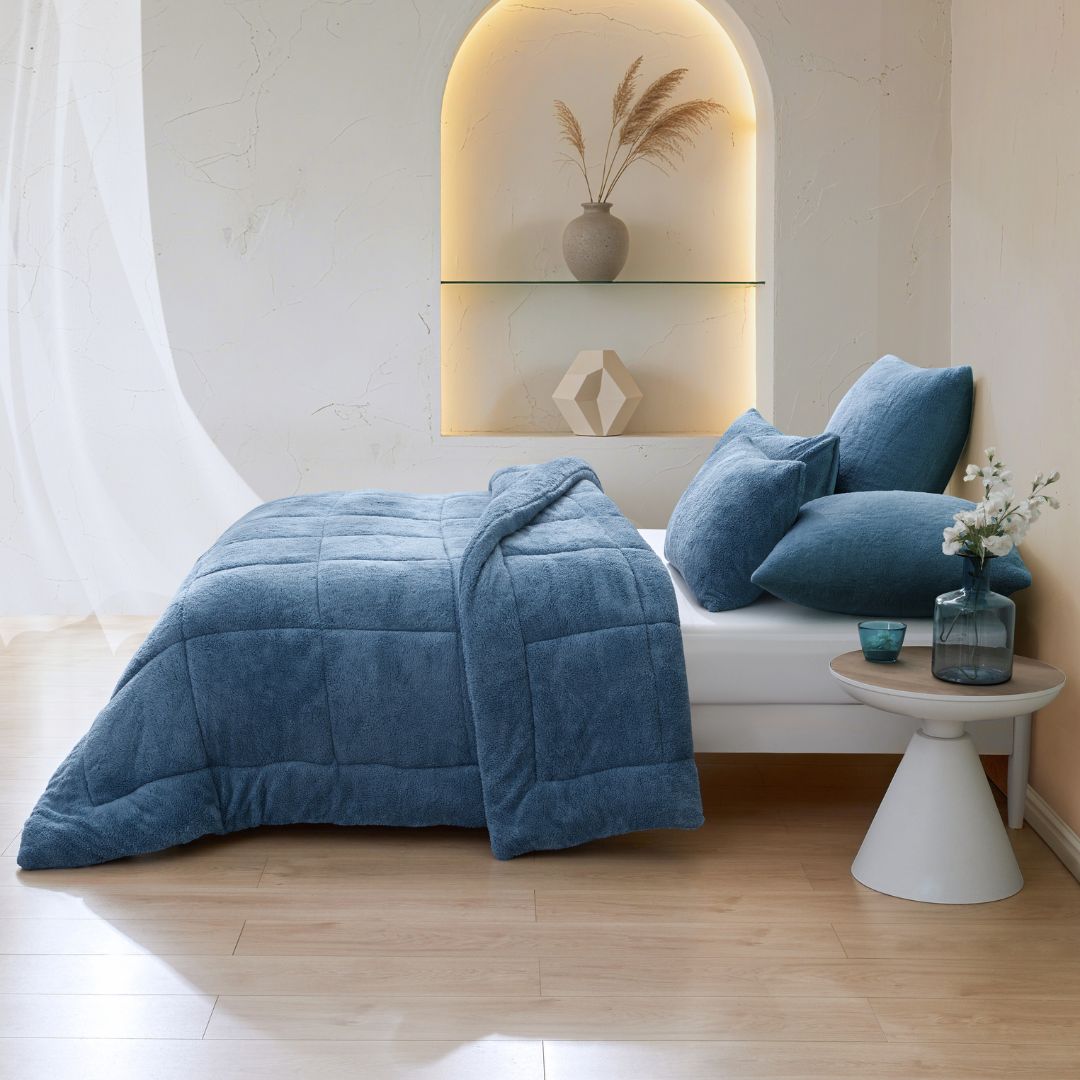 Blue textured comforter on a bed in a modern bedroom with a side table and decorative items.