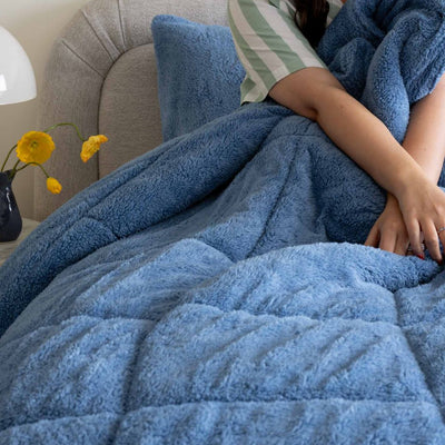 Person wrapped in a blue blanket on a couch with yellow flowers in the background