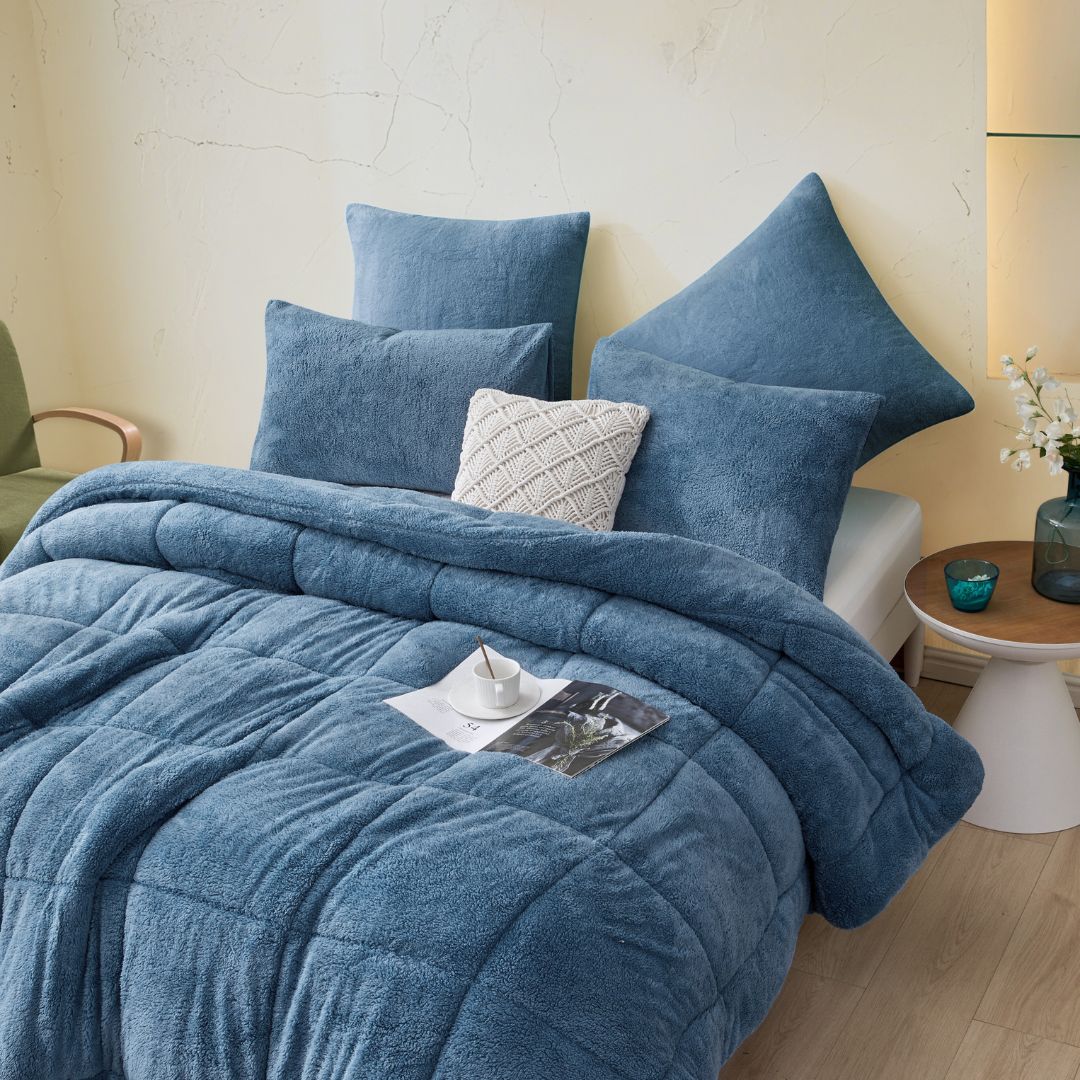 Blue textured comforter and pillows on a bed in a bedroom setting.
