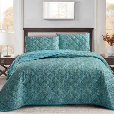 A bright bedroom features the Morgan and Reid Art Deco Coverlet Set in teal blue, with a quilted microfibre bedspread and matching pillows by Morgan and Reid, styled with a wooden headboard, bedside tables, lamp, and a window reflecting autumn trees.