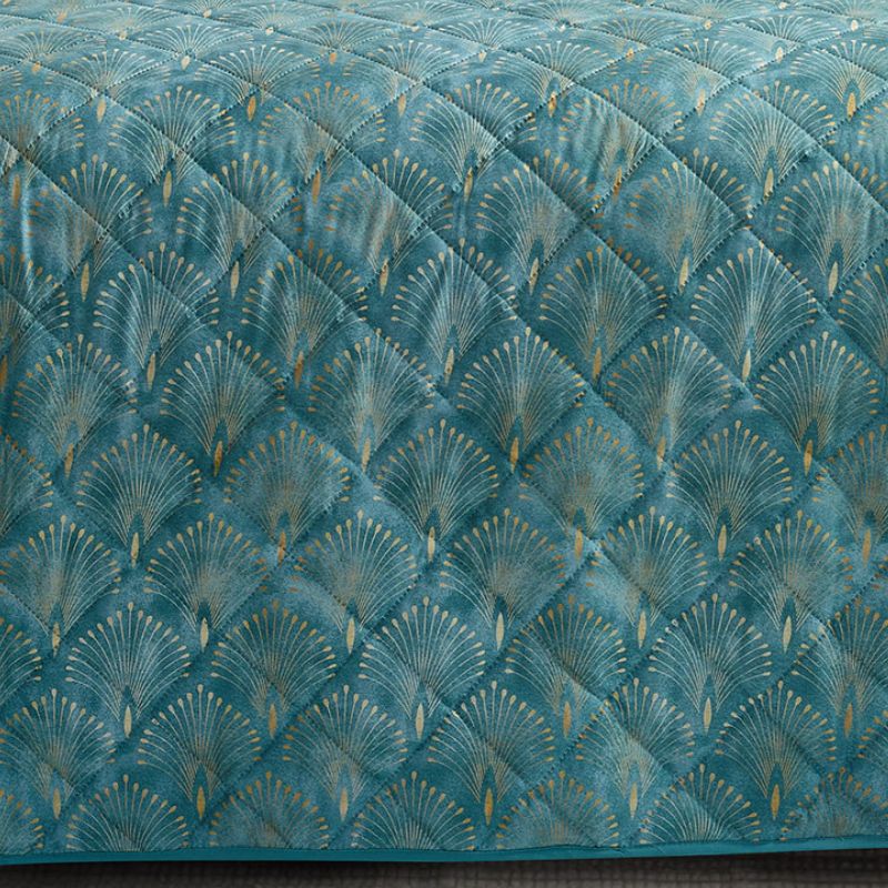 A bright bedroom features the Morgan and Reid Art Deco Coverlet Set in teal blue, with a quilted microfibre bedspread and matching pillows by Morgan and Reid, styled with a wooden headboard, bedside tables, lamp, and a window reflecting autumn trees.