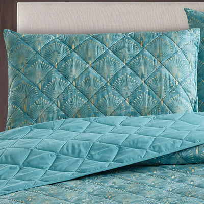 A bright bedroom features the Morgan and Reid Art Deco Coverlet Set in teal blue, with a quilted microfibre bedspread and matching pillows by Morgan and Reid, styled with a wooden headboard, bedside tables, lamp, and a window reflecting autumn trees.