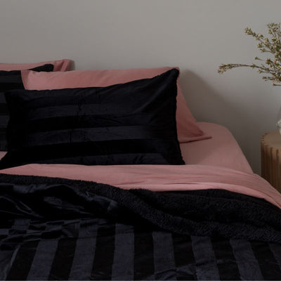 Bed with pink and black bedding against a neutral wall.