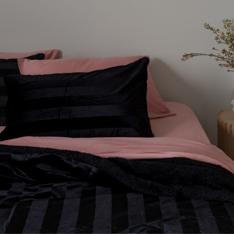 Bed with pink and black bedding against a neutral wall.