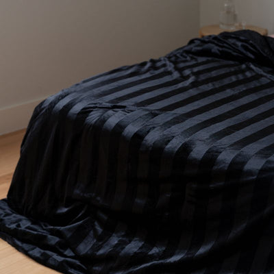 Black striped blanket on a bed in a room with neutral walls.