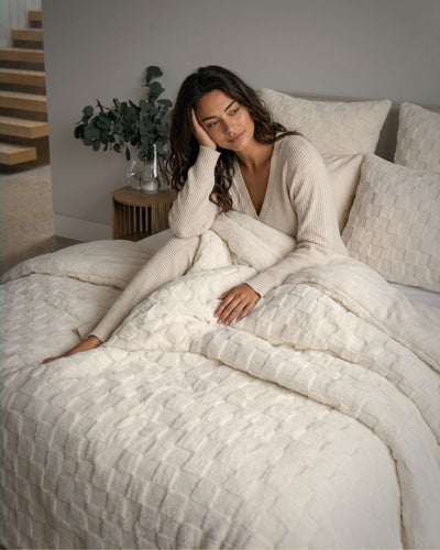 Woman in a white sweater sitting on a bed with textured bedding