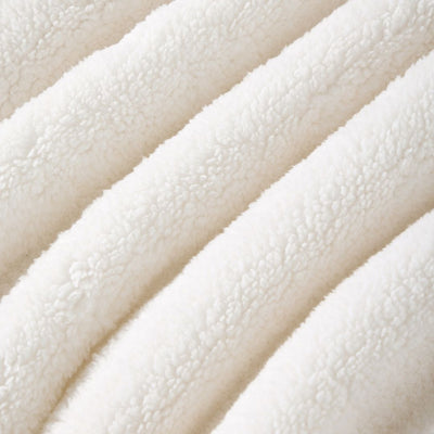 A neatly made bed showcases the Morgan and Reid Checkered Cream Snuggle Fleece Comforter Set with textured pillows, against a light wall, paired with a wooden headboard, bedside table, lamp, and a large leafy plant.