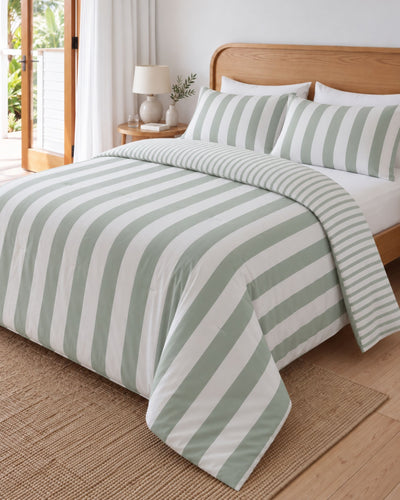 A bed dressed in a striped duvet cover and matching pillow shams with alternating sage green and white vertical stripes, styled in a bright bedroom with a wooden headboard, bedside lamp, and woven rug.