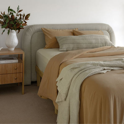 Neatly made bed with beige and brown bedding in a bedroom setting.