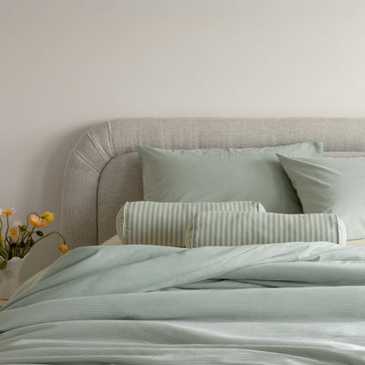 Bed with light blue bedding and pillows against a neutral wall.