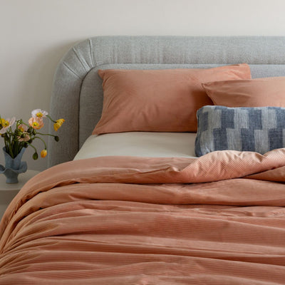 Bed with pink orange bedding and pillows, featuring a vase of flowers on the nightstand.