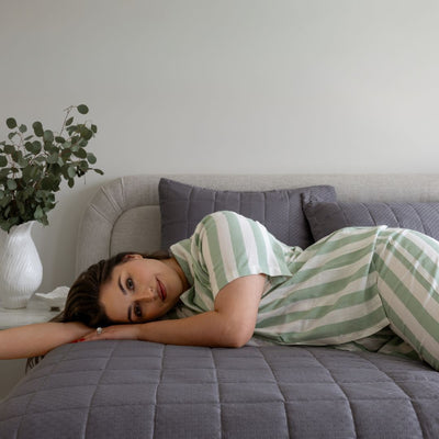Woman in a green and white striped dress lying on a gray couch with a plant in the background