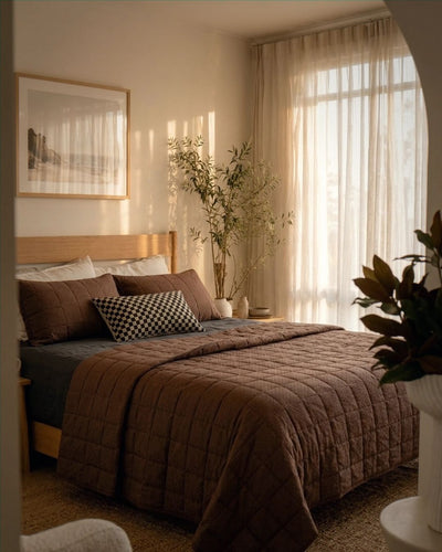 Cozy bedroom with brown bedding, wooden headboard, and large window with curtains.