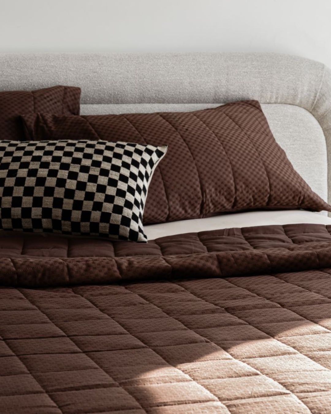 Brown quilted bedspread and pillows on a bed with a checkered pillow.