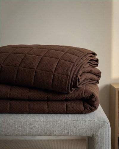Folded brown quilt on a bed in a softly lit room