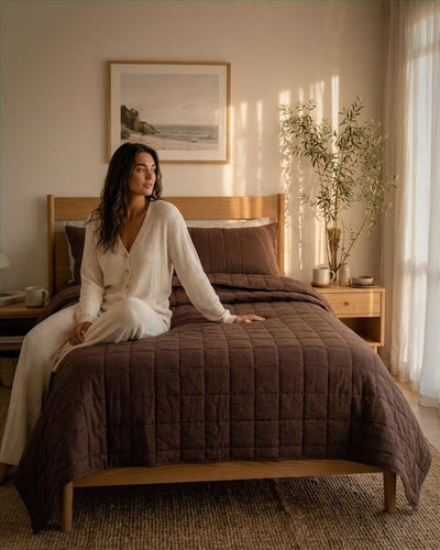 Woman sitting on a bed with brown quilt in a cozy bedroom