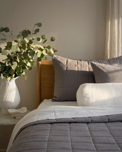 Bedroom with a bed featuring gray bedding and pillows, a vase with greenery on a nightstand.