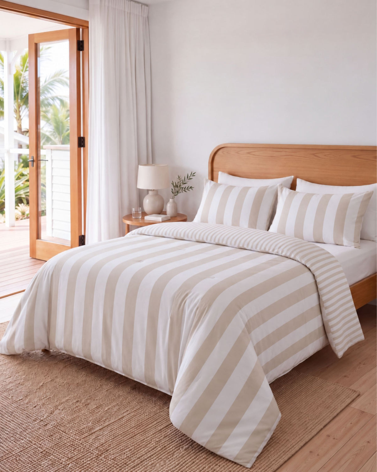 A neatly made bed in a bright bedroom with a beige and white striped duvet cover and matching pillow shams, set against a light wood headboard and a natural woven rug.
