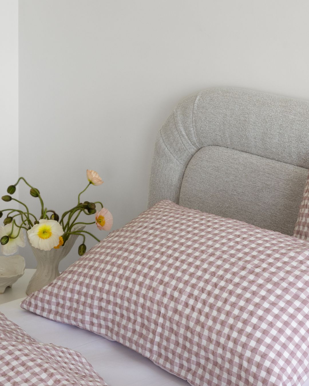 Checkered pillow on a bed with a vase of flowers in the background