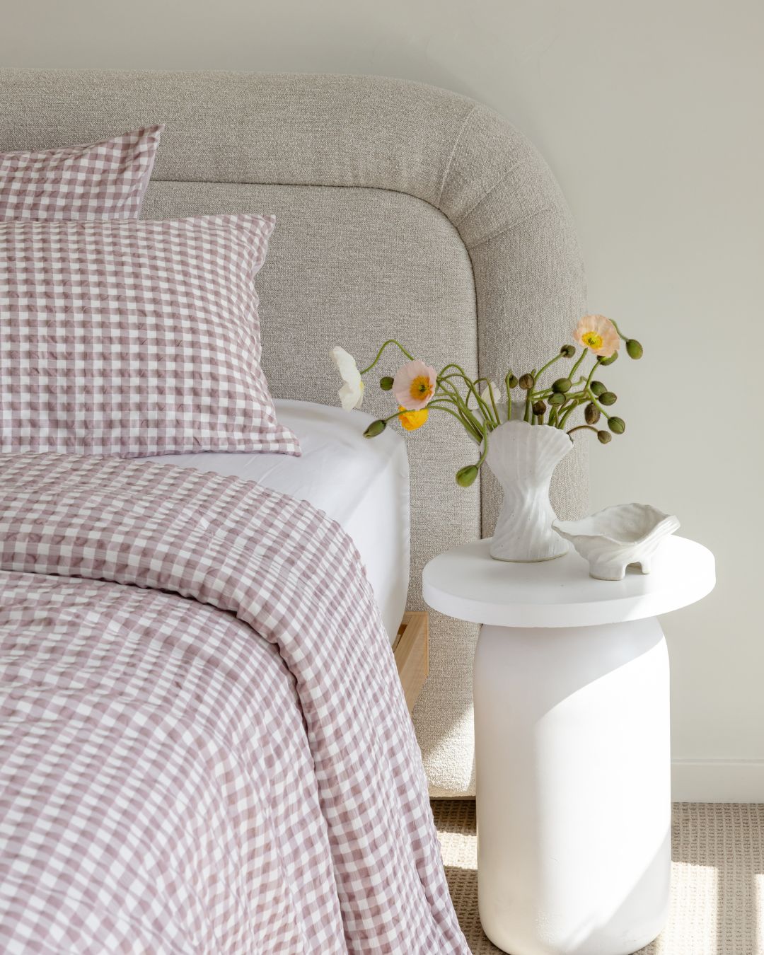 Bedroom with checkered bedding and a vase of flowers on a nightstand.