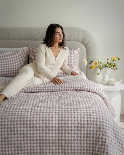 Woman sitting on a bed with checkered bedding in a cozy bedroom setting.