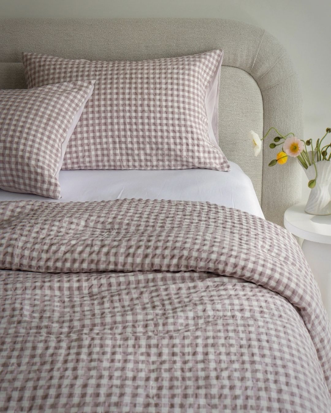 Checkered bedding set on a bed with a vase of flowers on a nightstand.