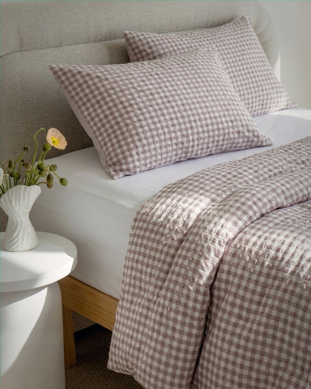 Bed with checkered bedding and pillows, next to a nightstand with a vase of flowers.