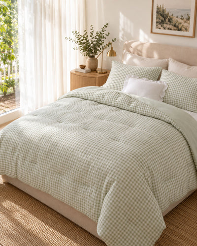 A neatly made bed in a bright bedroom setting, featuring a light sage green and white gingham checkered comforter and matching pillow shams.