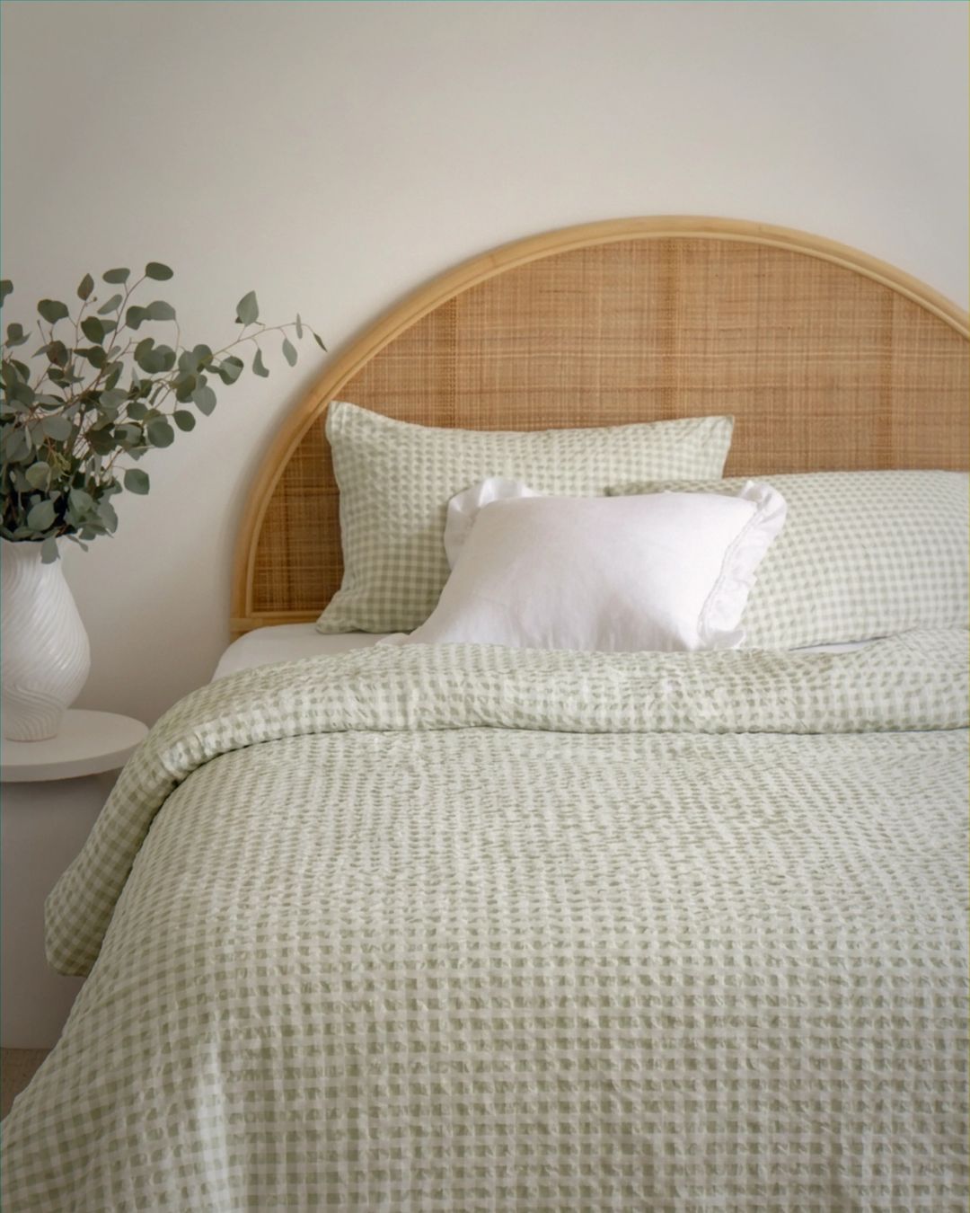 Bed with green checkered duvet and pillows, wooden headboard, and plant on nightstand.
