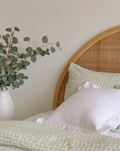 Bedroom with wicker headboard, green bedding, and eucalyptus plant.