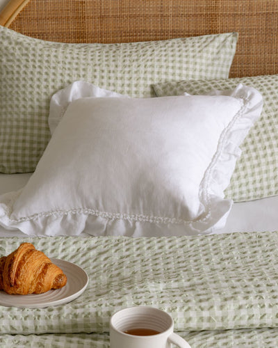 White pillow on a bed with green checkered sheets and a croissant on a plate.