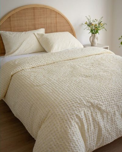 Neatly made bed with textured bedding, pillows, and a wooden headboard in a bedroom setting.
