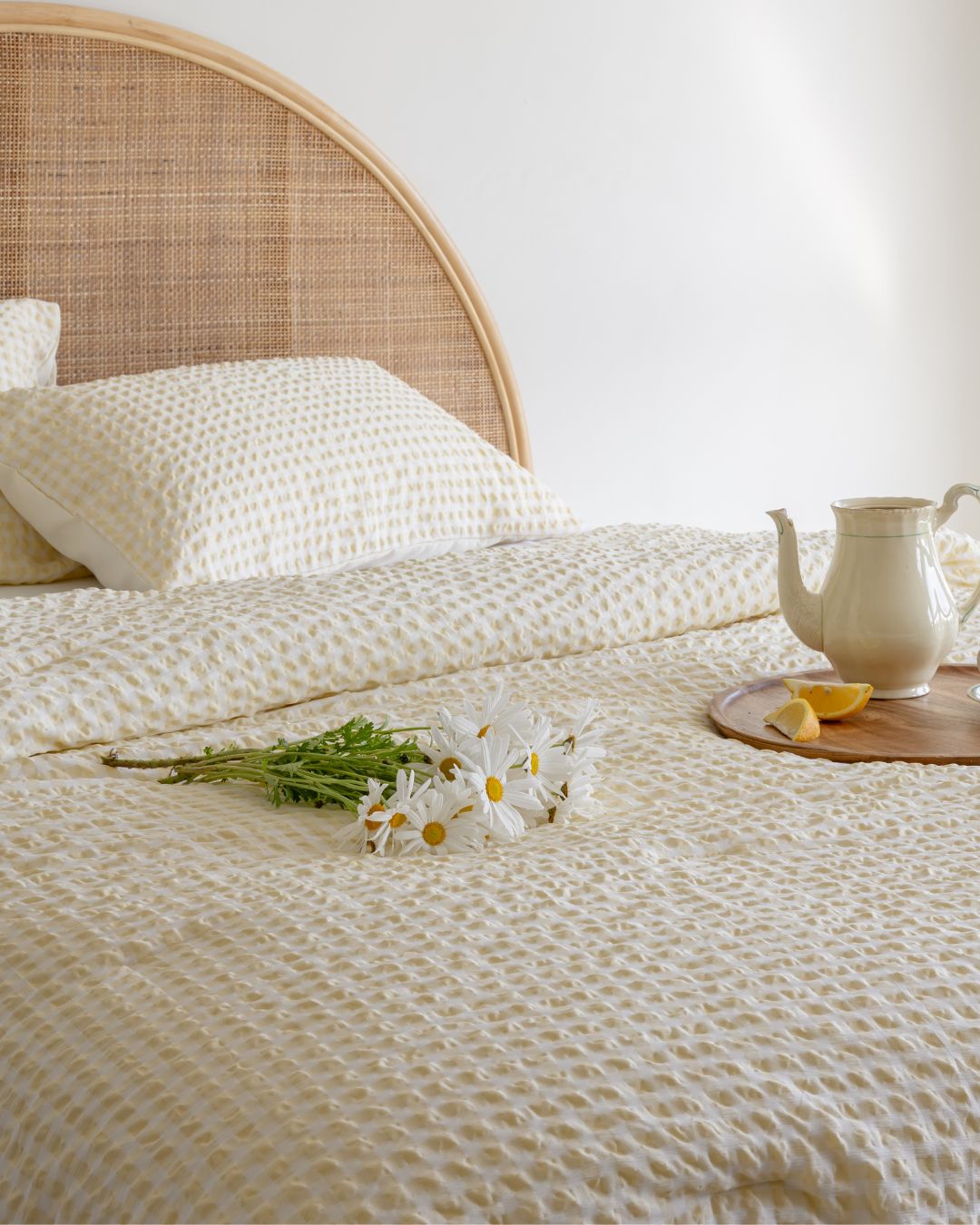 Bed with textured bedding, white pillows, and a small table with a teapot and lemon.