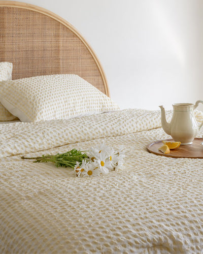 Bed with textured bedding, white pillows, and a small table with a teapot and lemon.