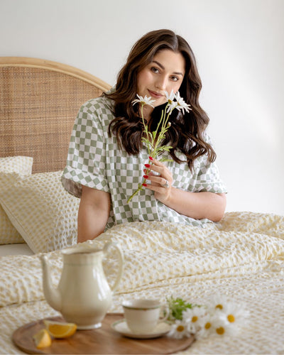 Woman holding flowers in a bedroom setting with a teapot and lemon on a wooden tray.
