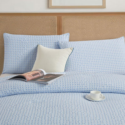Light blue textured bedding set with pillows and a magazine on a bed.