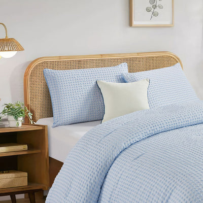 Bed with light blue bedding and pillows in a bedroom setting.