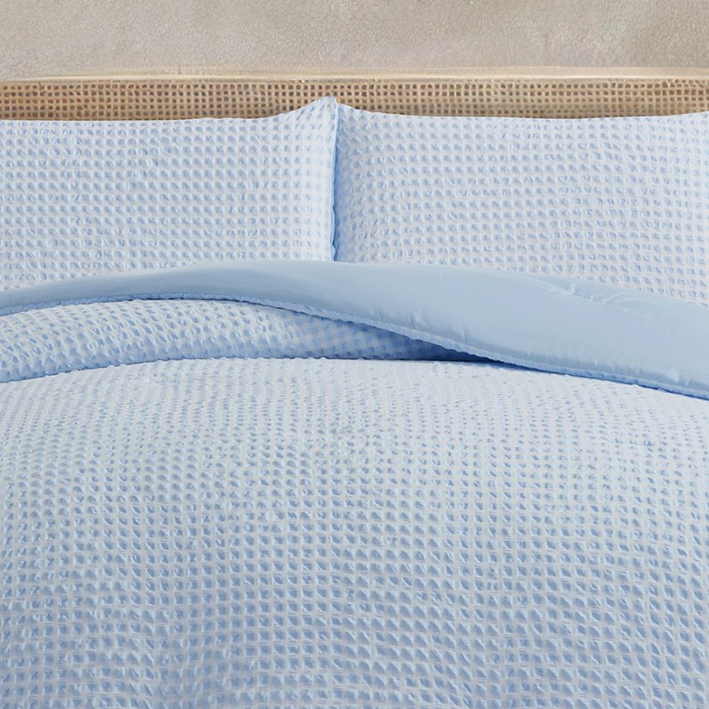 Light blue textured bedding set on a bed with a beige headboard.