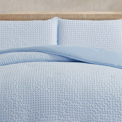 Light blue textured bedding set on a bed with a beige headboard.