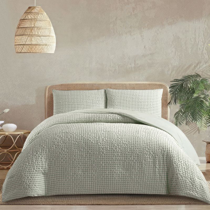 A calming bedroom displays the Morgan and Reid Eucalyptus Gingham Comforter Set on a neatly styled bed with matching pillowcases, rattan furniture, natural pendant lamp, indoor plant, and a woven rug.