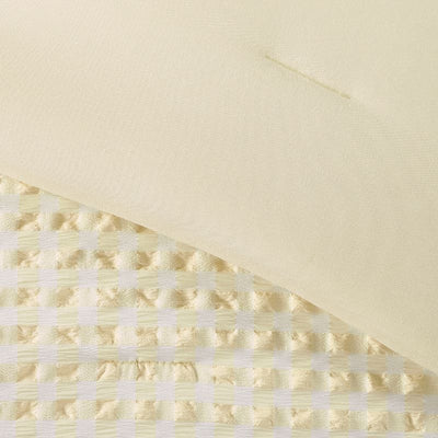 A modern bedroom features the Morgan and Reid Lemon Butter Gingham Comforter Set on a neatly made bed with matching pillowcases, rattan bedhead, neutral walls, woven pendant light, and a wooden side table with decorative accents.