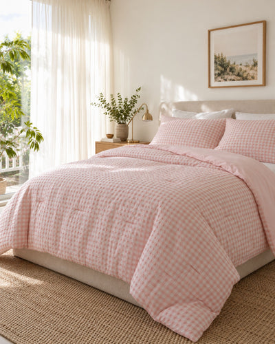 A pink and white gingham checkered comforter set with matching pillow shams on a bed in a bright, sunlit bedroom.