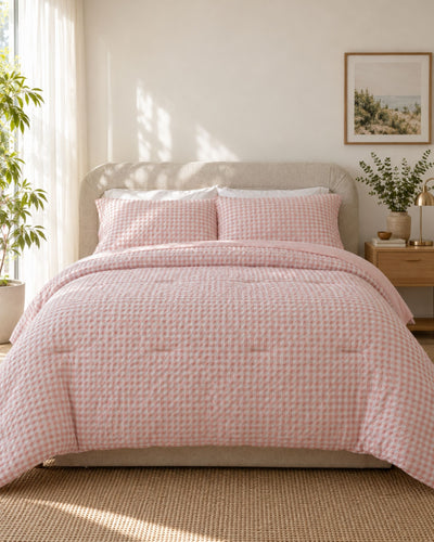 A pink and white gingham checkered comforter set with matching pillow shams on a bed in a bright, modern bedroom.