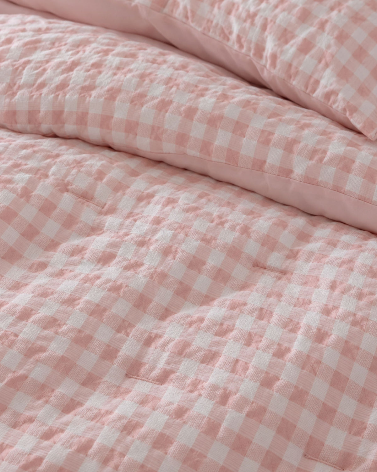 Pink and white gingham checkered quilted bedding, showing a close-up of the textured fabric and a matching pillowcase.
