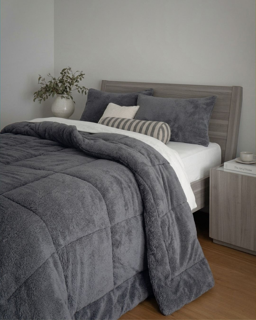 Gray comforter on a bed in a bedroom setting with a vase and plant.