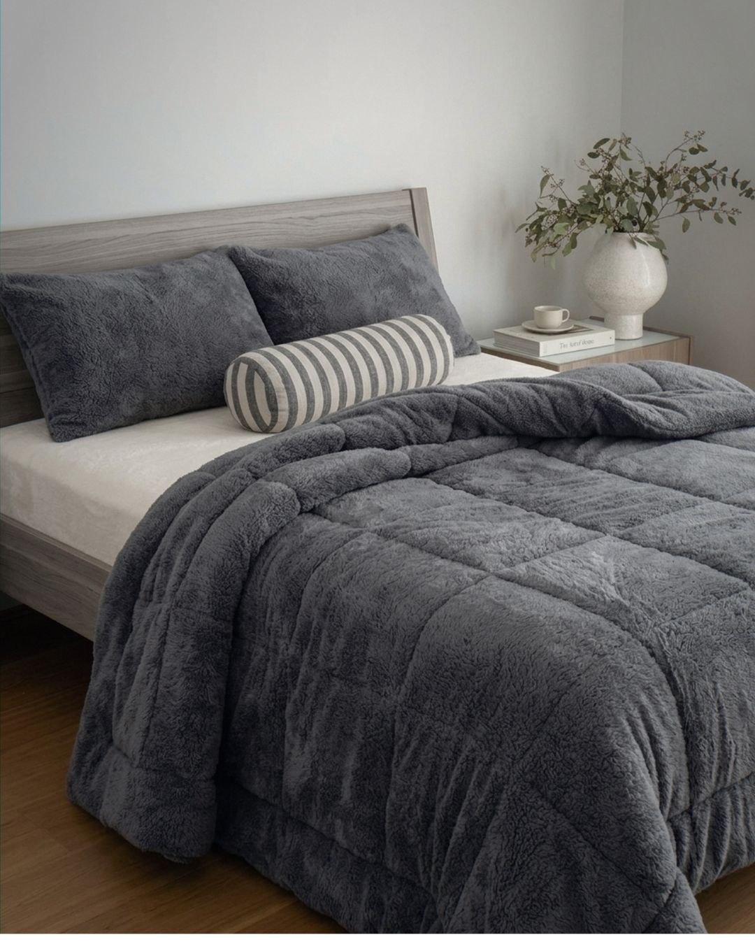 Gray textured comforter on a bed with pillows and a striped cylindrical pillow in a bedroom setting.
